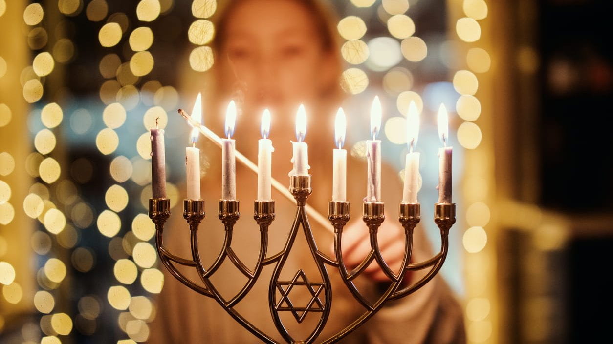 A girl lighting the Menorah candles with a long match for Hanukkah celebration over the holiday.